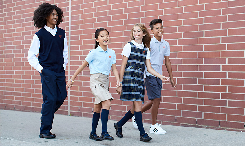 a group of four kids in uniform walking on a sidewalk